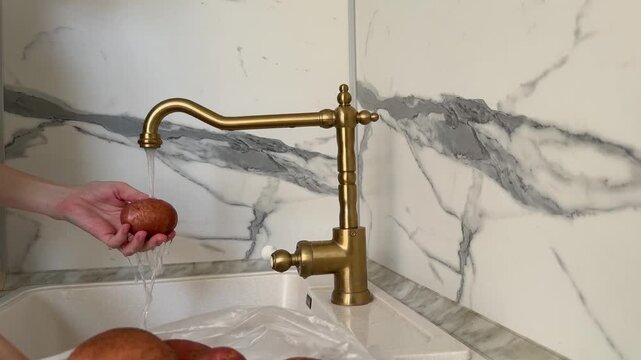 Woman washing raw potatoes with brush in kitchen sink 