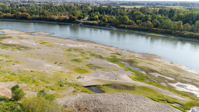 Aerial view of the Po river showing significant drought and low water levels with exposed sandy banks and sparse vegetation in Castelvetro Piacentino, Emilia-Romagna, Italy.