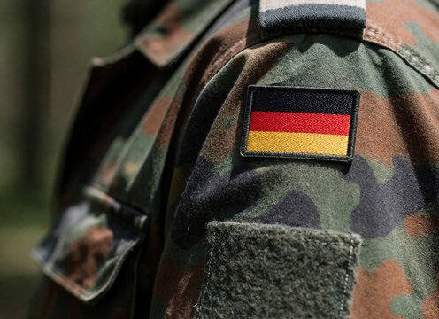 Close up view of German military uniform with camouflage pattern. German flag patch on soldier shoulder sleeve. Army combat clothing detail with national emblem. Patriotism, defense concept in
