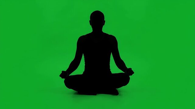 Silhouette of a person meditating in a lotus position against a vibrant green screen background, promoting relaxation and mindfulness.