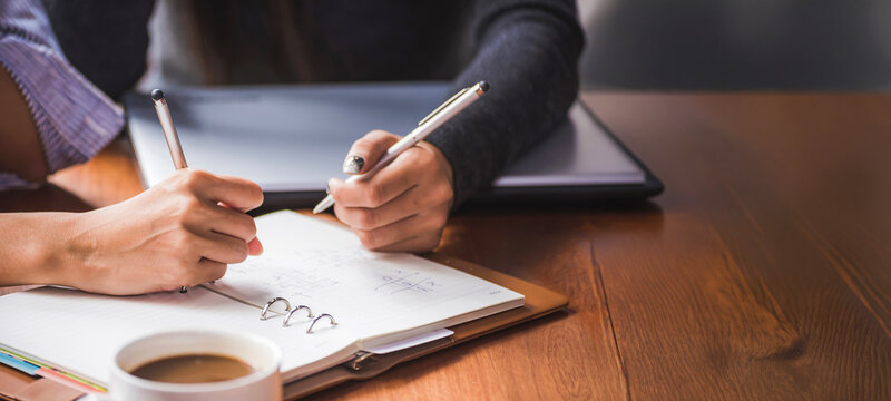 Hand of business people with pen and data sheet at meeting. Woman learning and reading a book together at coffee shop or cafe in the morning, vintage tone