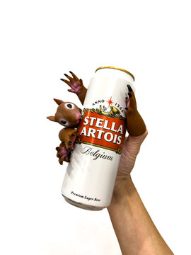 A hand wearing funny squirrel finger puppets holds a tall can of Stella Artois premium lager against a solid white background. Novosibirsk, Russia, on August 19, 2026