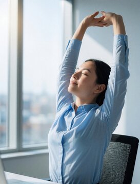 Young woman stretches arms overhead at office desk. Employee takes break for good posture and energy boost. Healthy habit for work productivity and wellbeing at desk.