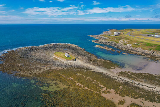Aerial view of St Cwyfan's Church situated on a small tidal island surrounded by the Irish Sea, with rocky shores and clear blue water in Ty Croes, Wales, United Kingdom.