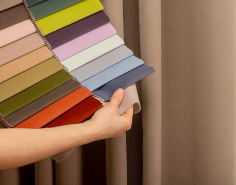 Textile material swatch fan held in decorator studio workspace. Hands showing colorful upholstery