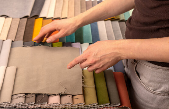 Upholstery swatch book selection for modern sofa design. Interior designer pointing at beige fabric