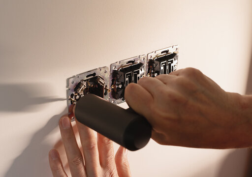 Wall socket outlet repair using power screwdriver in room. Electrician hands mounting metal triple