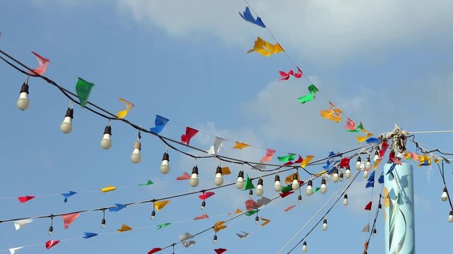 Colorful party bunting flags and string light bulbs hanging against blue sky at lake resort in Thailand