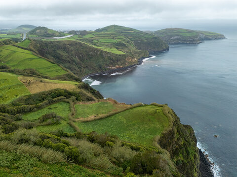 Aerial view of the lush green coastal cliffs and fields surrounding Miradouro de Santa Iria, overlooking the Atlantic Ocean in Porto Formoso, Acores, Portugal.