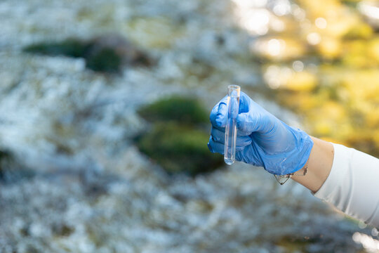 person in blue gloves holding glass tube with water sample outdoors testing for escherichia coli and gastrointestinal disease outbreak risk with copy space for banner design