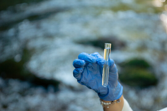 person in blue gloves holding glass tube with water sample outdoors testing for escherichia coli and gastrointestinal disease outbreak risk with copy space for banner design