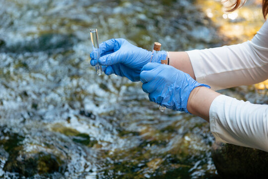 person in blue gloves holding glass tube with water sample outdoors testing for typhoid fever and coliform bacteria outbreak risk with copy space for banner design