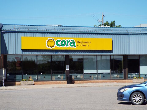 Gatineau, Quebec, Canada &ndash; June 26, 2026: A blue building features a bright yellow "Cora D&eacute;jeuners et d&icirc;ners" restaurant sign above large tinted glass windows at 200 Bd Gr&eacute;ber.
