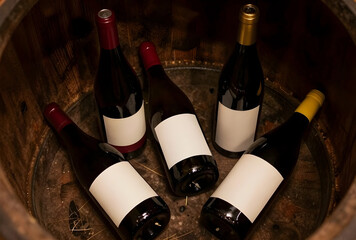 Naklejka premium Wine tasting and cellar storage concept, multiple bottles of red wine with blank labels in a rustic wooden barrel