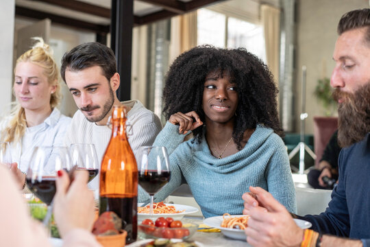 Young woman listens to friends during a relaxed multicultural dinner at home, sharing an attentive social moment. Gen z and millennial adults connect through conversation, food and friendship.