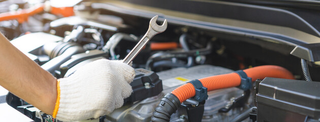 Fototapeta premium Auto mechanic hand holding a wrench during inspection and repair with electric hybrid car engine bay, professional vehicle maintenance service.
