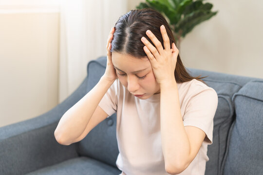 Depressed anxiety asian young woman frustrated hand on head, touching her temples, suffering stressed, sick, tired, crisis on sofa from headache, migraine pain tension problem health care concept.