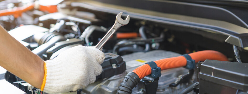 Auto mechanic hand holding a wrench during inspection and repair with electric hybrid car engine bay, professional vehicle maintenance service.