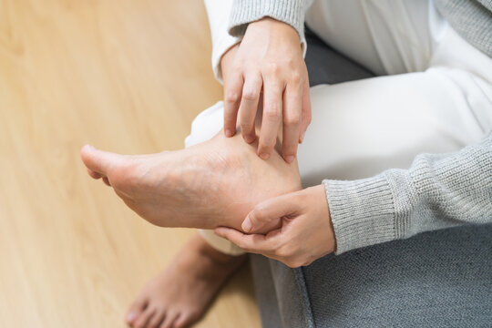 Foot pain, Smelly feet woman hand scratch feet, itch foot, problem itchy skin sitting on sofa at home, dermatitis from fungus, fungal bacterial infection, allergic reaction, eczema. Foot care concept.
