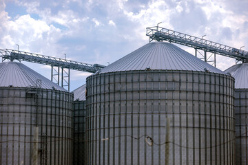 Large metal grain silos against a cloudy sky, showcasing contemporary agricultural storage and industrial infrastructure. © Alexandra