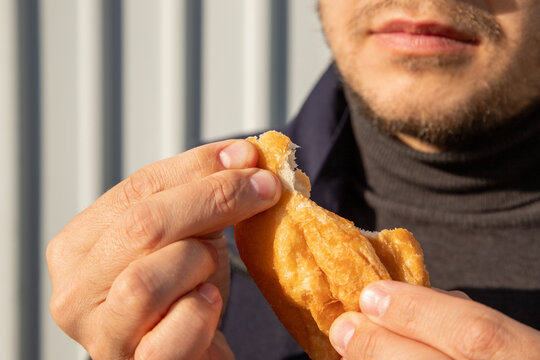 Man eating a golden fried pastry by hand. Close-up snack moment highlighting crispy dough, traditional baursak and hearty homemade food concept.