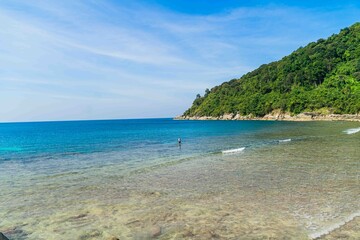 Fototapeta premium The backdrop of the sky is a pristine tropical coastline with rocks, palm trees, turquoise sea, and a relaxing beach atmosphere. Merlin Snorkelling Beach, uncrowded Patong, Phuket, Thailand.