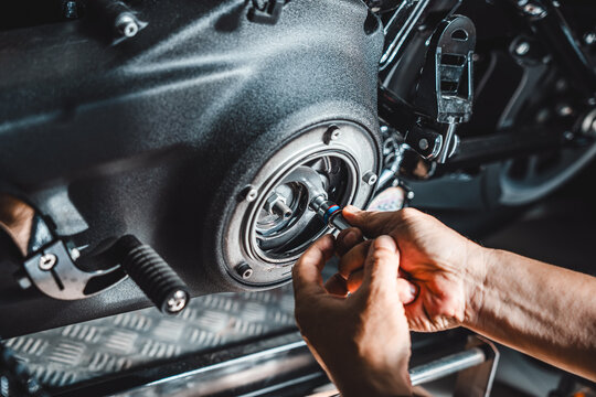 Close-up of a technician's hands using a hand ratchet tool to service and adjust motorcycle primary drive clutch assembly inside a garage workshop.