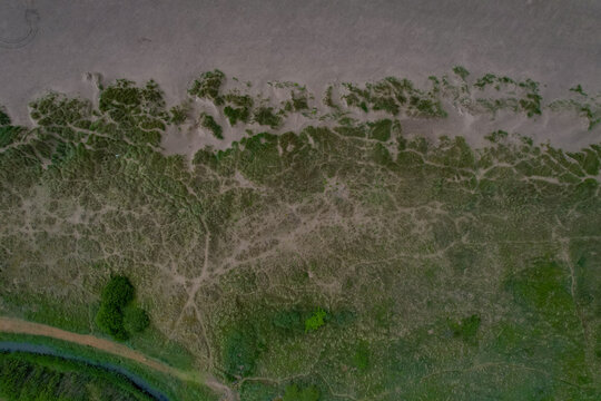Aerial view of sand dunes covered in coastal grasses meeting the sandy beach in Porthmadog, Wales, United Kingdom.