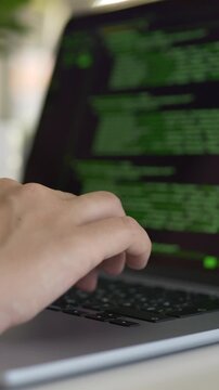 Developer works on laptop displaying colorful green source code in modern workspace. Coding, software creation, cybersecurity and startup development concept focused on building digital products. 