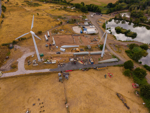 Aerial view of Mal Leisure at Seighford Lakes showing wind turbine construction with blades on the ground, heavy machinery, and a nearby lake in Stafford, England, United Kingdom.
