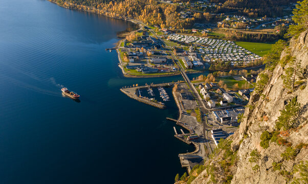 Aerial view of Valldal, featuring a cargo ship in the fjord, a marina, and surrounding autumn forests and steep cliffs in Sylte, More og Romsdal, Norway.