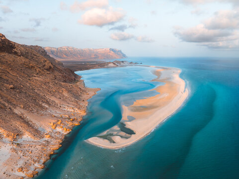 Aerial view of Detwah Lagoon Ramsar Site featuring turquoise waters, white sandbars, and rocky cliffs under a clear sky, Socotra, Yemen.