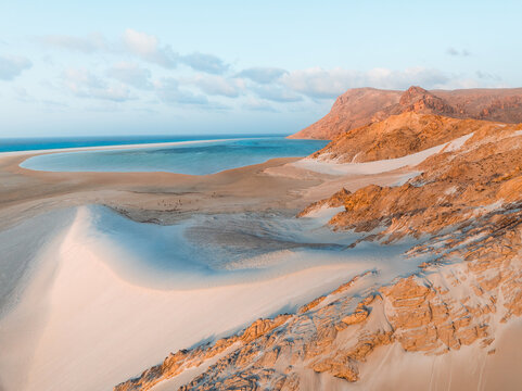Aerial view of Detwah Lagoon Ramsar Site featuring pristine white sand dunes, turquoise waters, and rugged rocky cliffs in Socotra, Yemen.