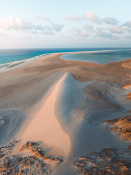 Aerial view of Detwah Lagoon Ramsar Site featuring expansive white sand dunes, turquoise waters, and gentle golden hour light on the coast of Socotra, Yemen.