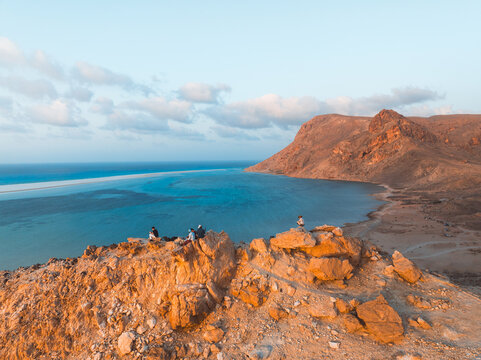 Aerial view of Detwah Lagoon Ramsar Site with people sitting on rocky cliffs overlooking the turquoise water and arid landscape in Socotra, Yemen.