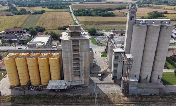 Aerial view of a large industrial grain mill complex with yellow and concrete silos, featuring a truck loading grain in the yard surrounded by fields in Smederevo, Podunavlje District, Serbia.