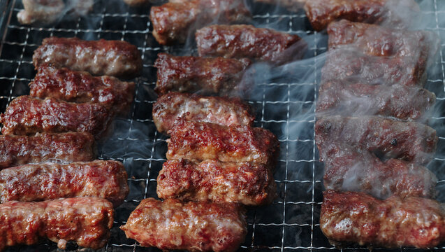 Close view of cevapi sizzling on a smoky barbecue grill. Juicy Balkan minced meat sausages show rich texture, rustic cooking and outdoor food culture