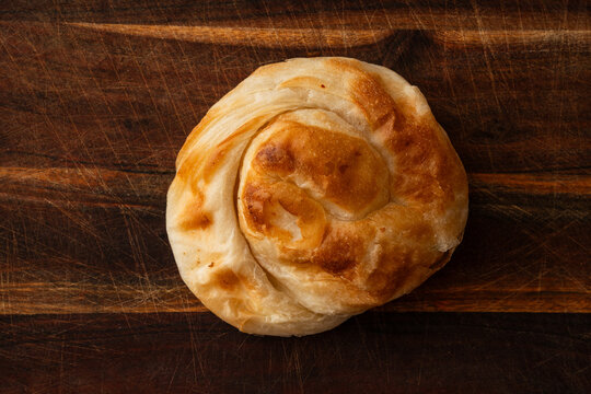 Burek, a typical Balkan baked product made with thin layers of puff pastry and a cheese filling. Photographed on a wooden surface.