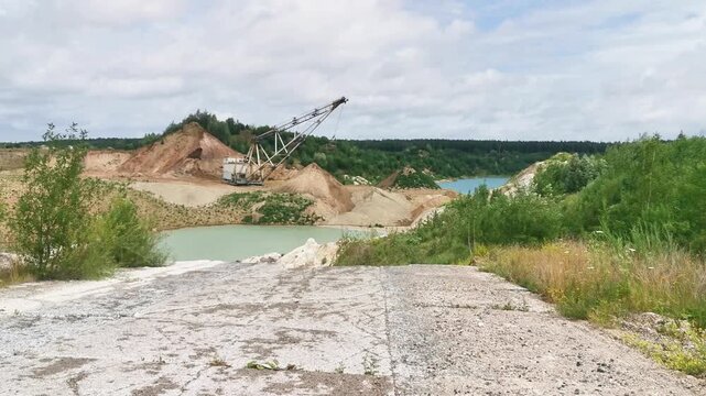 Industrial sand quarry with dragline excavator by turquoise water and greenery  