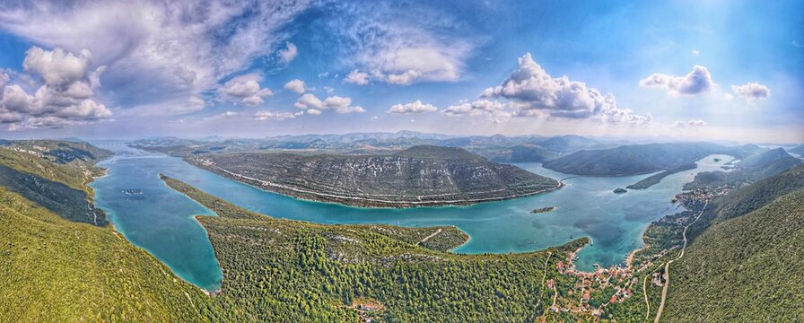 Aerial view of Mali Ston Bay featuring turquoise waters, surrounding lush green hills, rocky terrain, and the coastal village of Ston, Croatia.