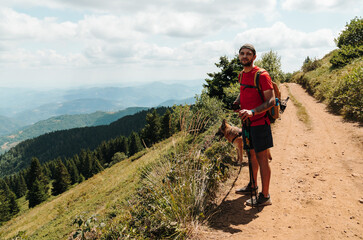 A hiker with a German Shepherd pauses on a mountain trail in Kopaonik, Serbia. The scene suits adventure travel, hiking, pet tourism and active lifestyle themes © Ekaterina