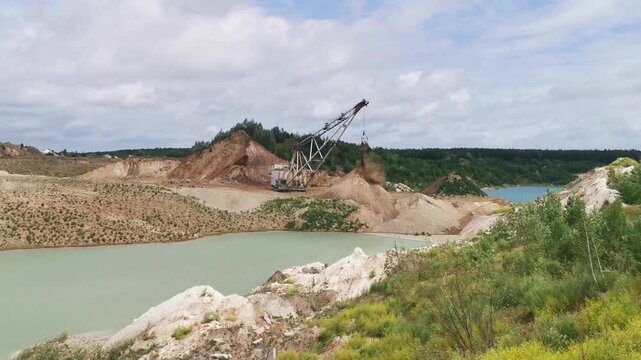 Large excavator operating at open-pit mine near water and forest in summer  