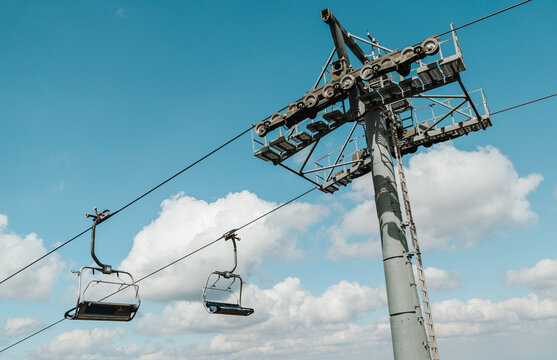 Empty chairlift seats pass a steel support tower in Kopaonik, Serbia. The ski lift structure is framed by blue sky and large summer clouds