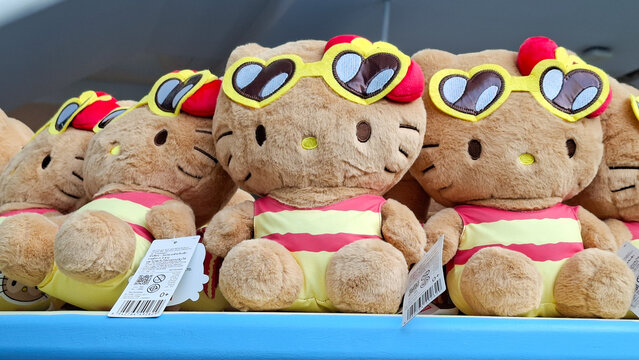 close up row of tan hello kitty sanrio plush dolls in red yellow striped swimsuits with yellow heart sunglasses lined up on store shelf display on August 17, 2026 in Bangkok, Thailand.
