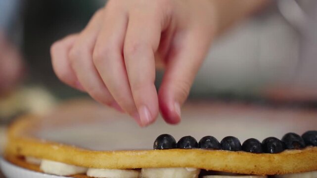 Child's hand decorating cake with blueberry halves close up