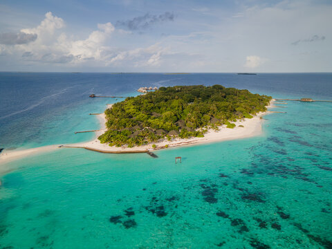 Aerial view of Meedhupparu island surrounded by turquoise lagoon, white sandy beaches, lush tropical vegetation, and overwater bungalows in Raa Atoll, Raa Atoll, Maldives.