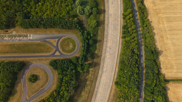 Aerial view of Millbrook Proving Ground featuring a circular vehicle testing track, curved roads, forest, and adjacent agricultural fields in Bedford, England, United Kingdom.