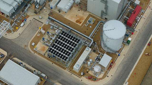 Aerial view of Millbrook Power Plant featuring a large storage tank, cooling fan arrays, and industrial infrastructure in Stewartby, England, United Kingdom.