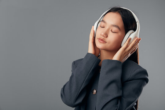 Young woman wearing headphones and closed eyes listening to music or podcast with peaceful expression on gray background in studio for relaxation and sound enjoyment.