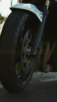 Close-up cinematic sequence of a modern sport motorcycle wheel and rider foot on footpeg, highlighting tire tread, brake disc, chain and performance details on asphalt road